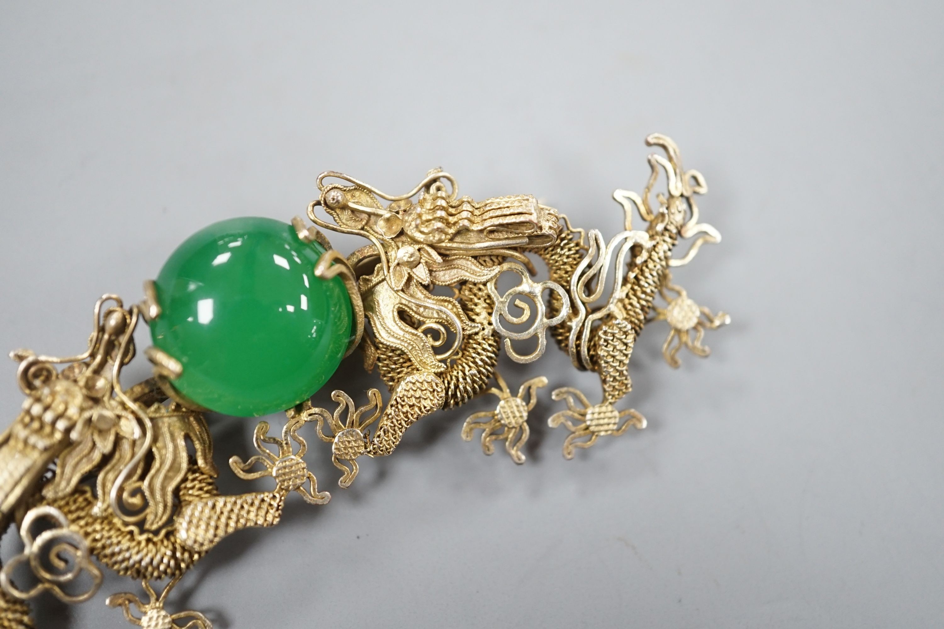 A Chinese gilt white metal and green cabochon stone set filigree dragon brooch, 88mm.